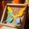 A radiant butterfly in full color — wings of gold, blue, and yellow spread in shimmering flight.
